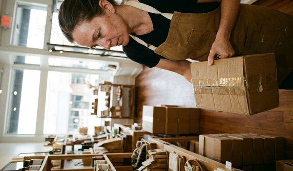 Small business owner in a work apron stocking retail store shelves with inventory boxes while preparing for the busy season