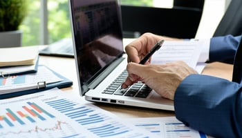 A business owner working on financial forecasting with a laptop and financial documents.