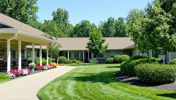 The image depicts a serene and inviting assisted living facility surrounded by lush greenery. 