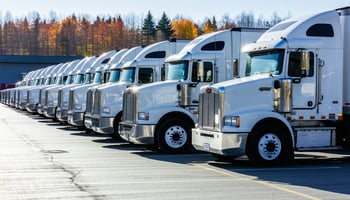 A modern trucking fleet lined up in a well-organized logistics yard, showcasing several large trucks parked in a row.