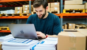 A business owner reviewing inventory with a laptop and financial documents.