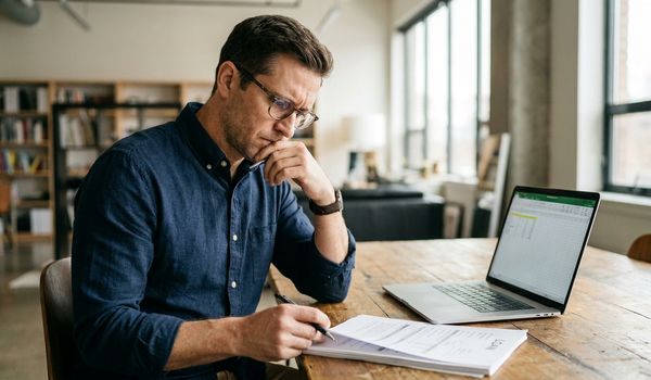 Small business owner at a wooden desk in a bright modern office reviewing loan documents with a laptop, comparing fixed and variable rate business loan options