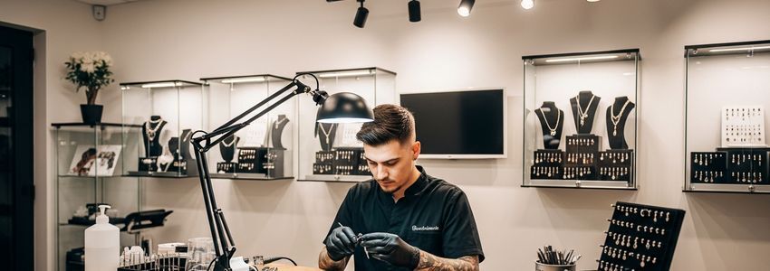 Professional piercing studio interior showing a piercing artist at work with display cases and equipment