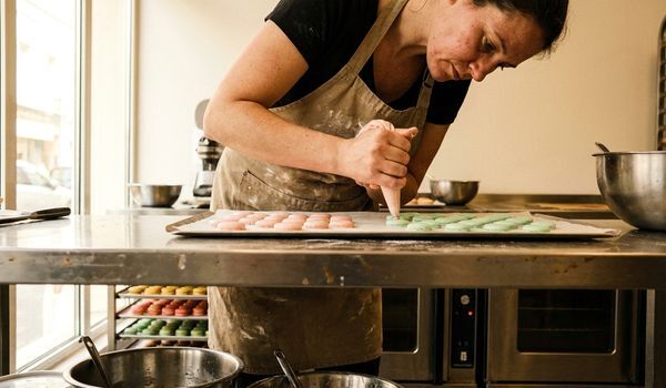 French macaron baker arranging colorful macarons in a commercial bakery display case