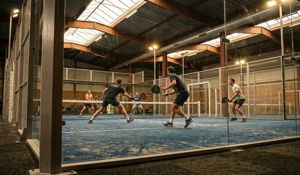 Four athletes playing a padel match on a glass-walled indoor court at a modern padel club
