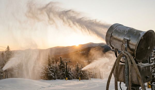 Snowmaking fan guns producing machine-made snow at a ski resort during golden sunrise