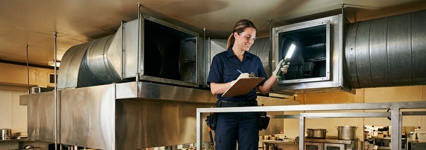 Commercial hood cleaning technician inspecting kitchen exhaust ductwork with professional cleaning equipment