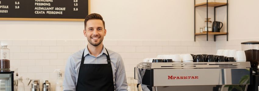 Coffee shop owner standing at counter beside commercial espresso machine
