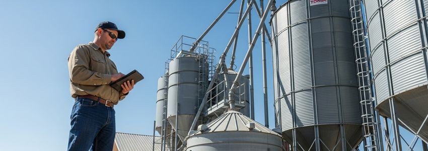 Farmer reviewing grain dryer financing options near grain bins and dryer system