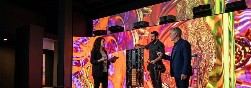Business owner and technician reviewing immersive art installation equipment financing beside a colorful projection-mapped exhibit wall