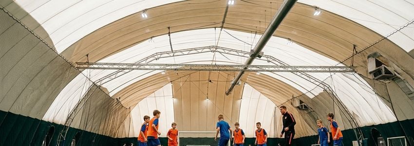 Wide interior view of an indoor sports dome with artificial turf field and netting in a professional athletic training facility