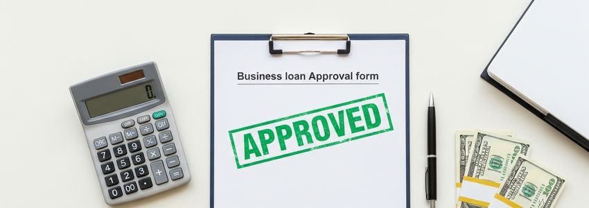 Business loan approval documents with a credit line application, calculator, and cash on a professional office desk