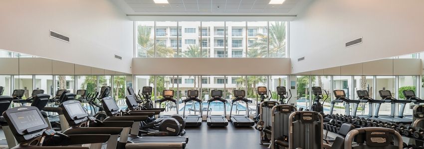 Resort fitness center with modern commercial exercise equipment and pool area visible through large windows