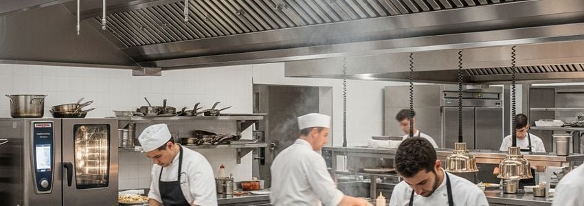 Professional commercial kitchen with stainless steel equipment and chefs working