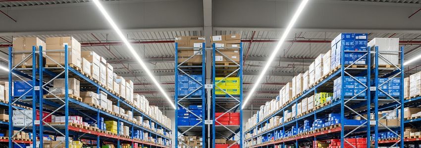 Organized commercial warehouse with rows of blue shelving stocked with colorful inventory boxes representing supplier supply chain management