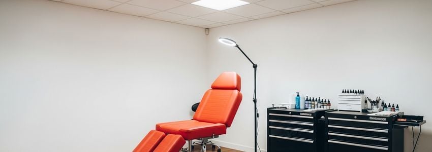 Professional tattoo studio interior with hydraulic client chair, organized supply workstation, and professional lighting setup