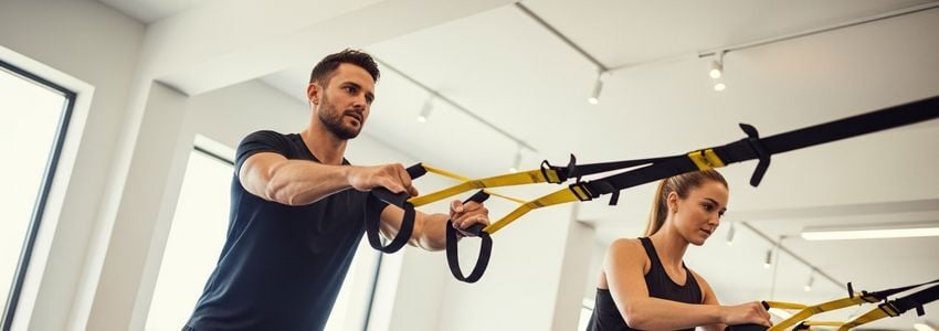 Fitness instructor demonstrating TRX suspension training equipment to a client in a modern commercial gym