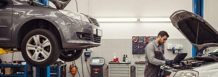 Auto mechanic working on vehicle in professional repair shop with hydraulic lift and diagnostic equipment