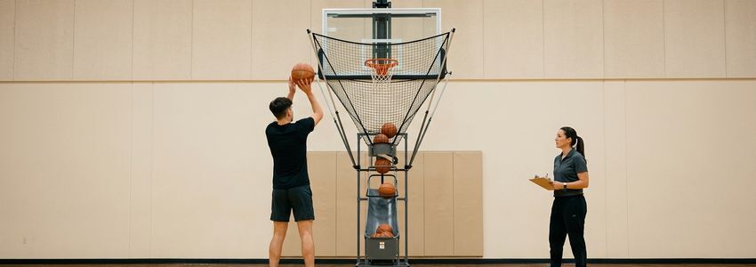 Basketball coach and player using an automated shooting machine in a commercial training facility