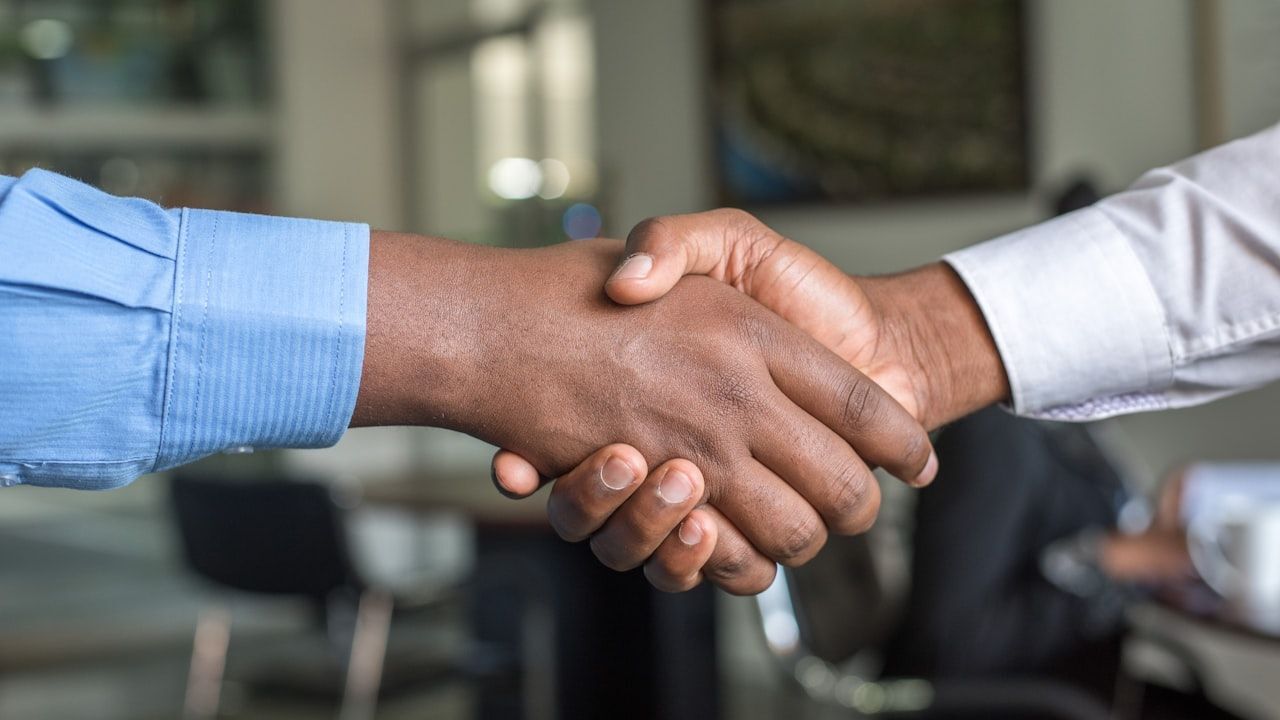 Small business owner and equipment dealer shaking hands in front of industrial machinery at a warehouse
