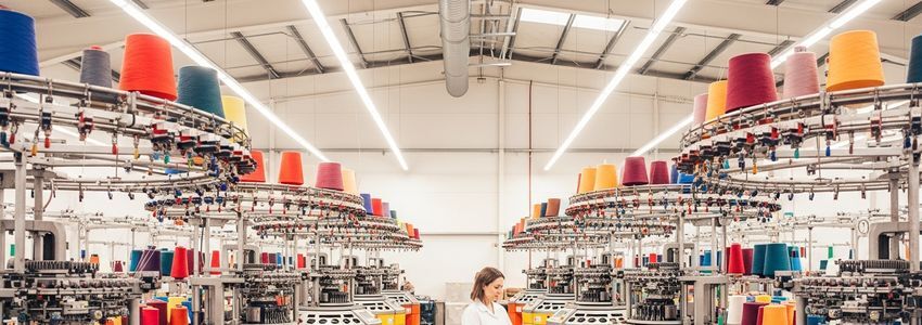 Commercial knitting machines on a textile manufacturing floor with colorful yarn spools