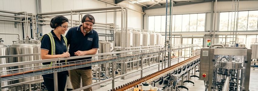 Beverage production line workers reviewing kombucha bottling equipment in a commercial facility