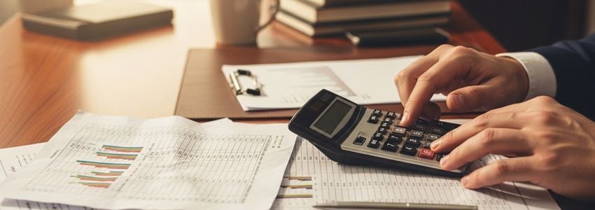 Business professional analyzing financial documents and calculator to compare merchant cash advance vs business loan costs