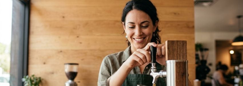 Barista pouring nitro cold brew coffee from a nitrogen tap system at a coffee shop counter