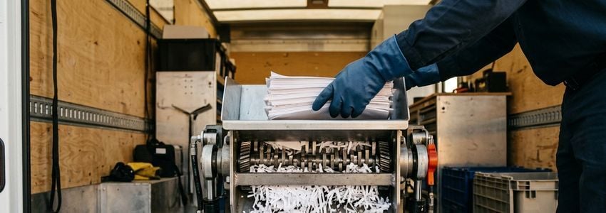 Worker loading documents into an industrial shredder mounted inside a mobile shredding truck