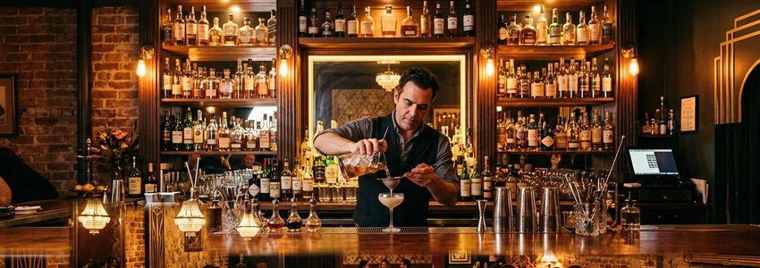 Bartender preparing craft cocktails at a dimly lit speakeasy-style bar with vintage decor
