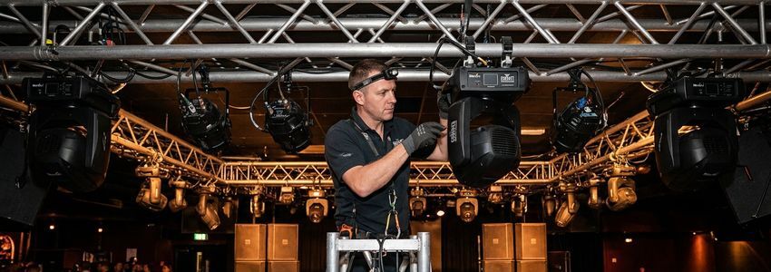 Technician installing professional DJ stage lighting fixtures on truss rigging at an event venue
